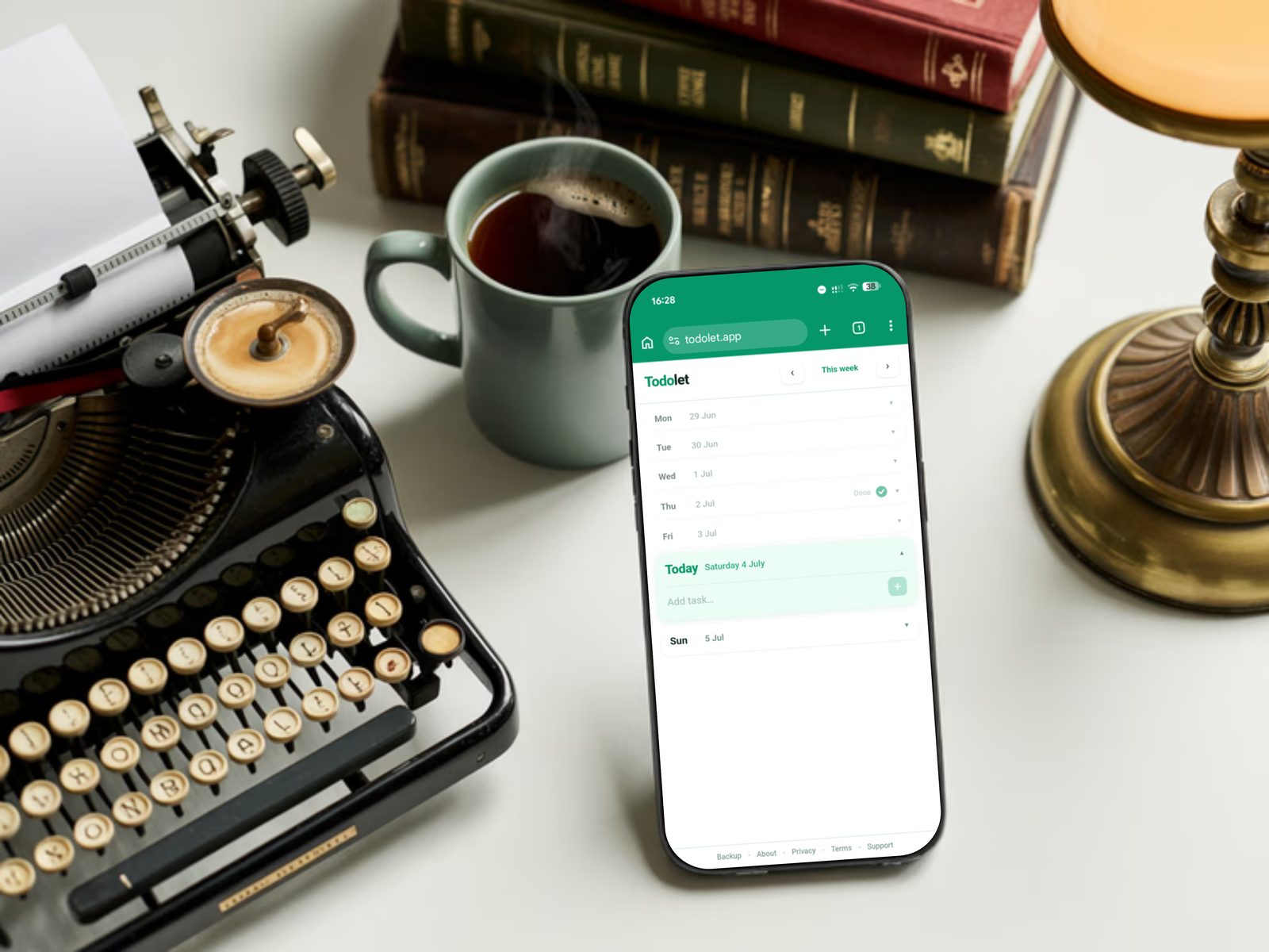 Todolet on a phone beside a vintage typewriter, stacked books, and a mug of coffee